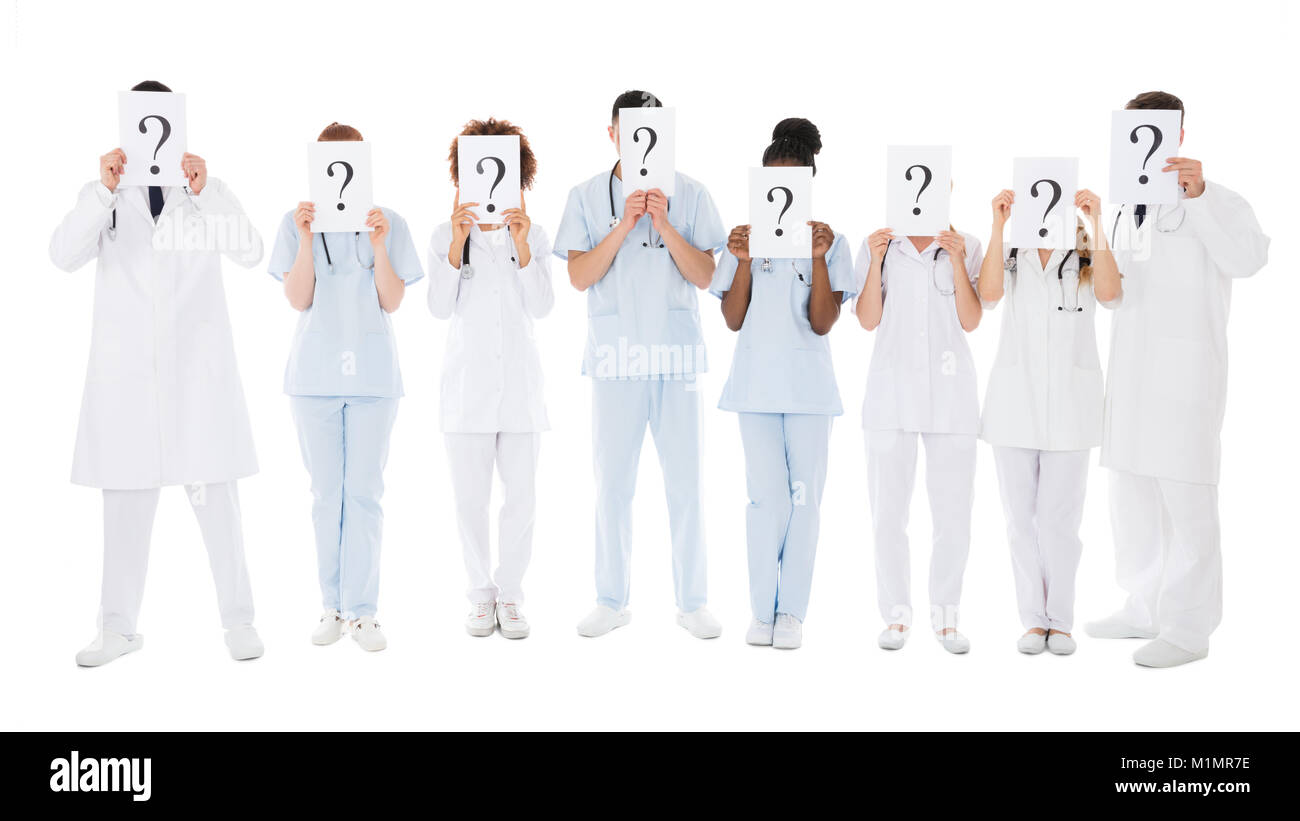 Il gruppo di medici e multirazziale di nascondersi dietro il punto interrogativo segno su sfondo bianco Foto Stock