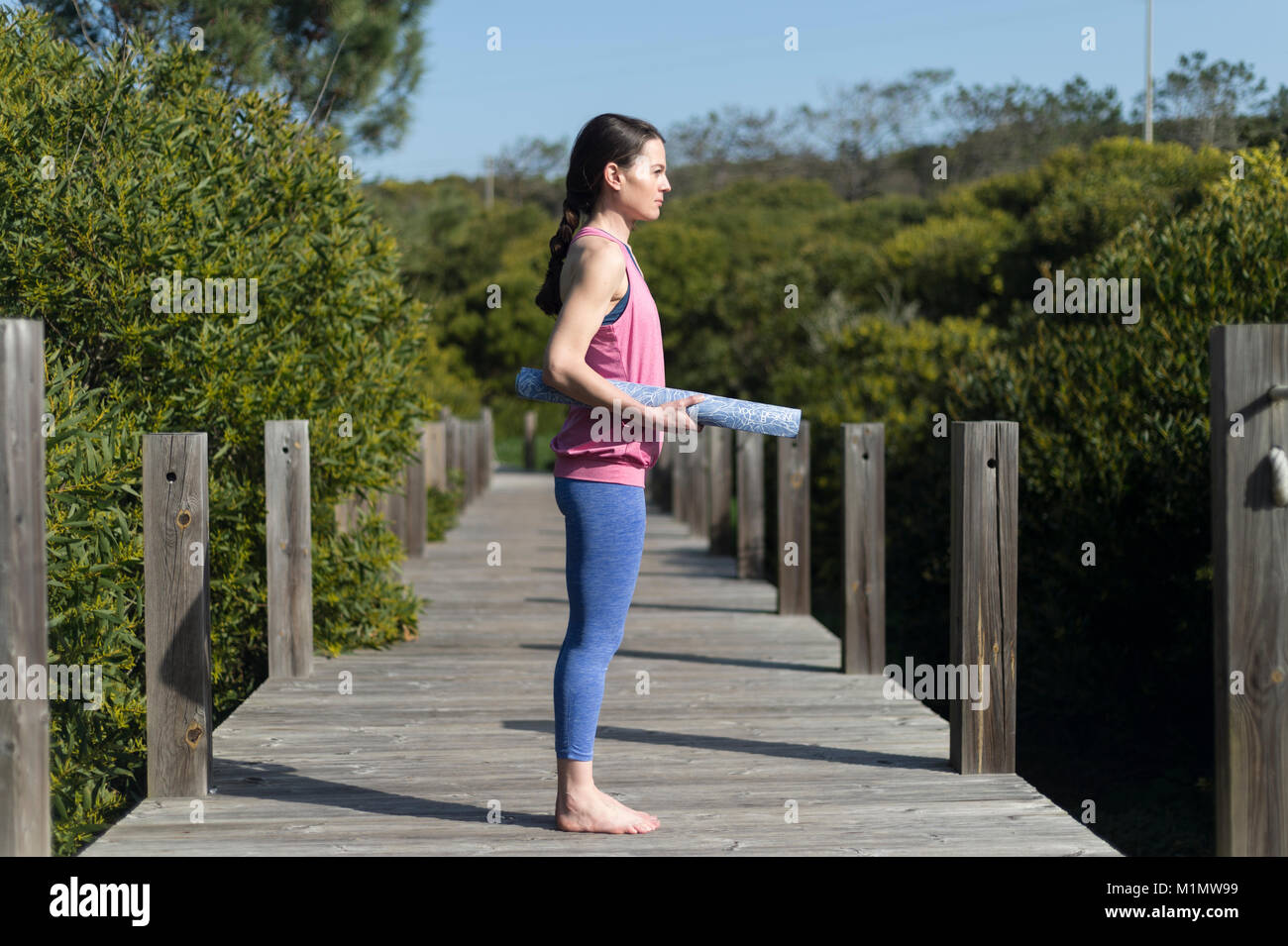 La donna che porta un arrotolato materassino yoga, esterno su un ponte di legno. Foto Stock