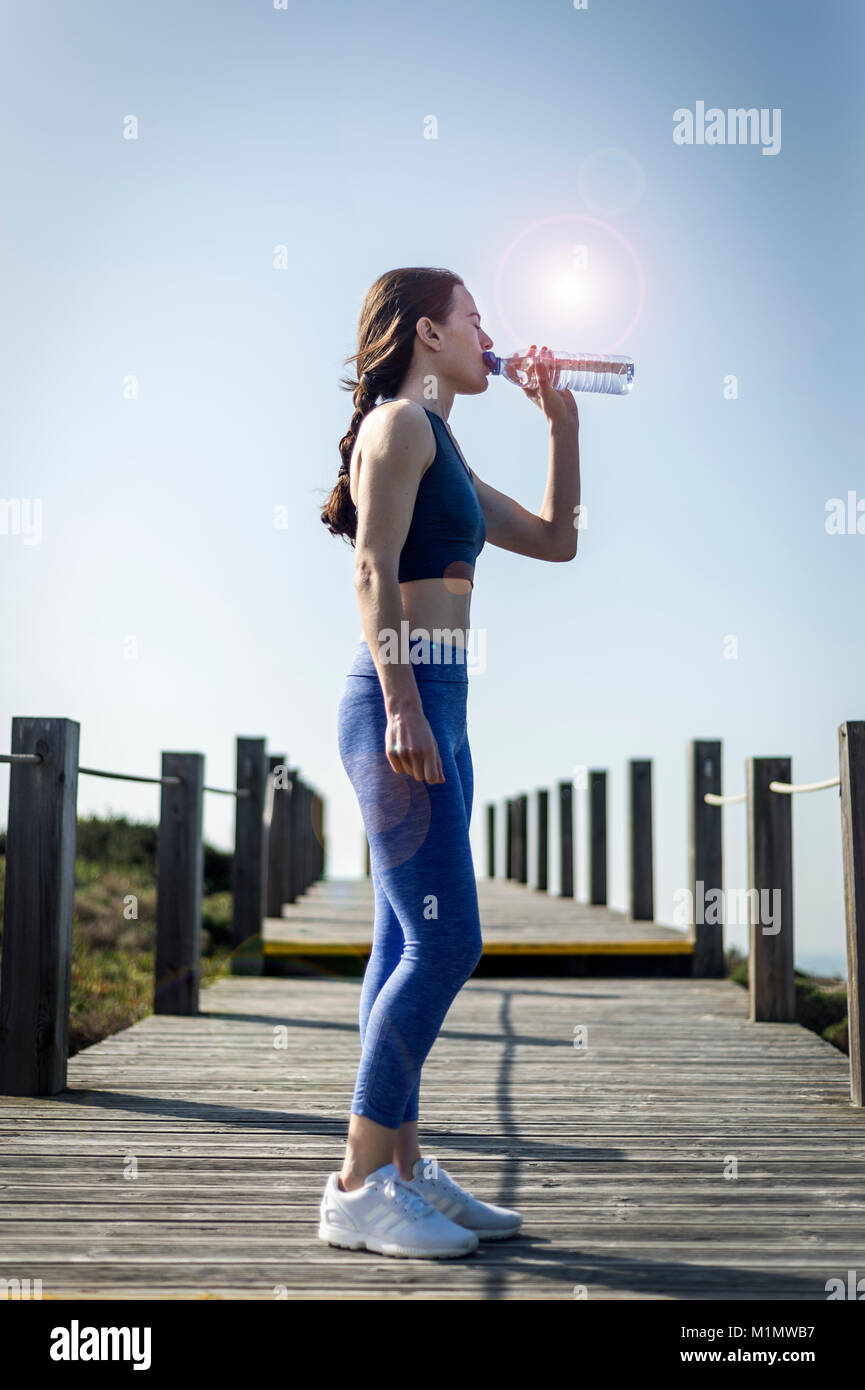 Donna di bere acqua da una bottiglia dopo aver acceso e di esercizio, lens flare. Foto Stock