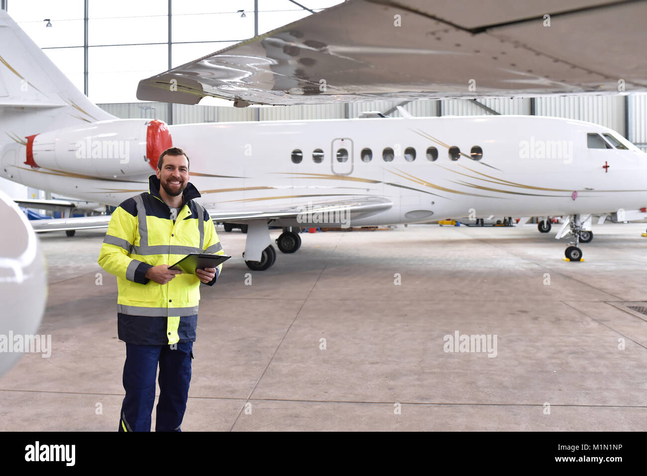 Ritratto di un meccanico aeronautico in un hangar con getti all'aeroporto - controllo del velivolo per la sicurezza e la funzione tecnica Foto Stock