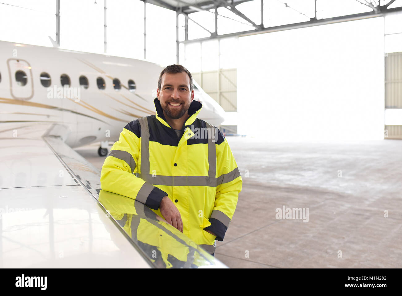 Ritratto di un meccanico aeronautico in un hangar con getti all'aeroporto - controllo del velivolo per la sicurezza e la funzione tecnica Foto Stock