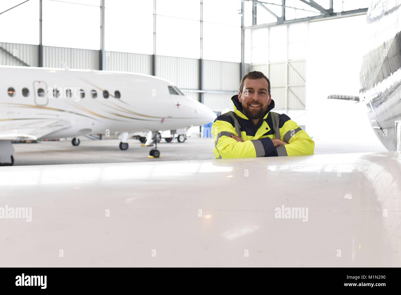 Ritratto di un meccanico aeronautico in un hangar con getti all'aeroporto - controllo del velivolo per la sicurezza e la funzione tecnica Foto Stock