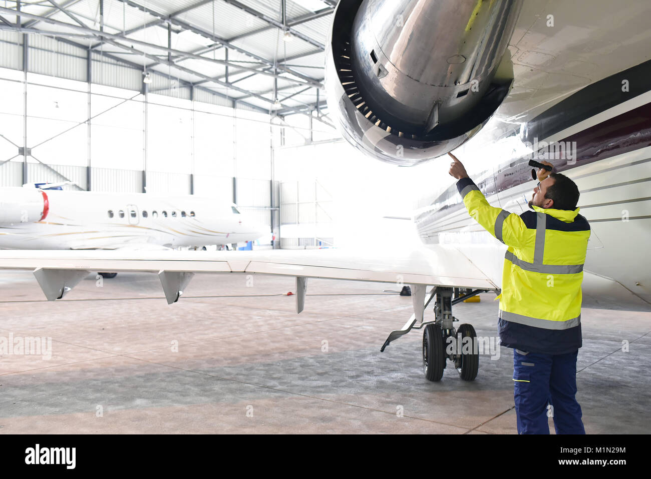 Meccanico aeronautico/ equipaggio a terra ispeziona e controlla la turbina di un jet in un hangar in aeroporto Foto Stock