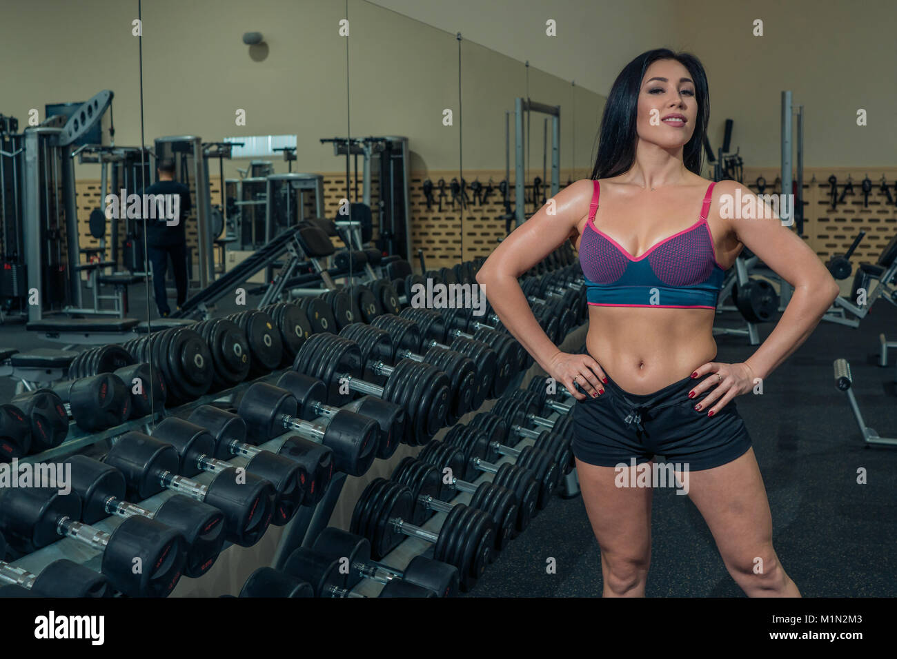 Bella donna modello di fitness che pongono sullo sfondo dei pesi nella palestra Foto Stock