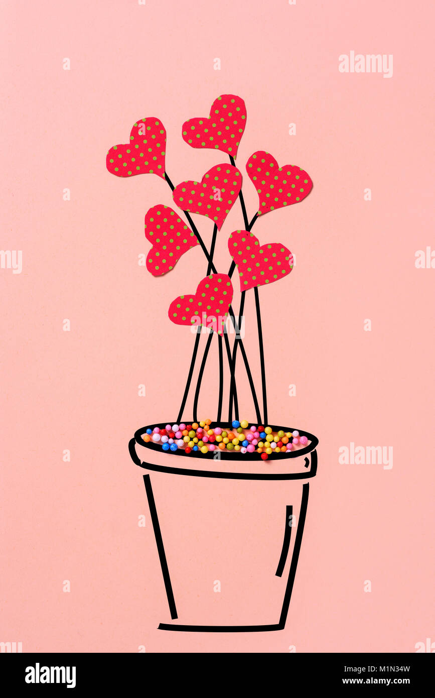 Un disegno di una pianta in un vaso di piante con alcuni cuori tagliati di un rosso papper modellato con puntini verdi che simulano fiori, su un pallido sfondo rosa Foto Stock