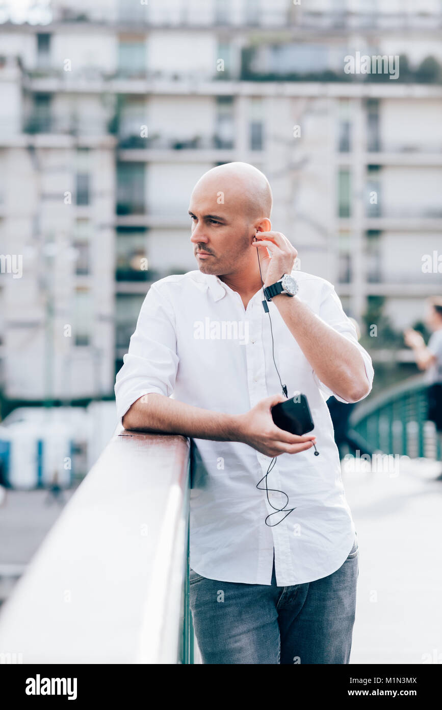 Giovane uomo caucasico ascoltando la musica con gli auricolari e smart phone tenere in mano all'aperto in città - audio, playlist, concetto rilassante Foto Stock