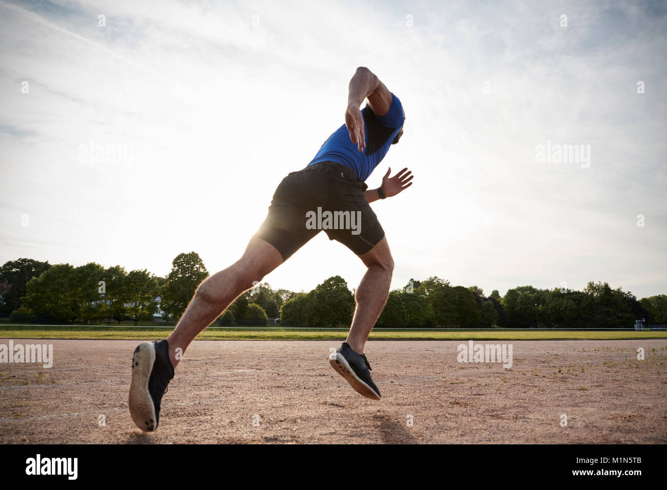 Giovane maschio atleta che corre in corrispondenza di una via a basso angolo di visione Foto Stock