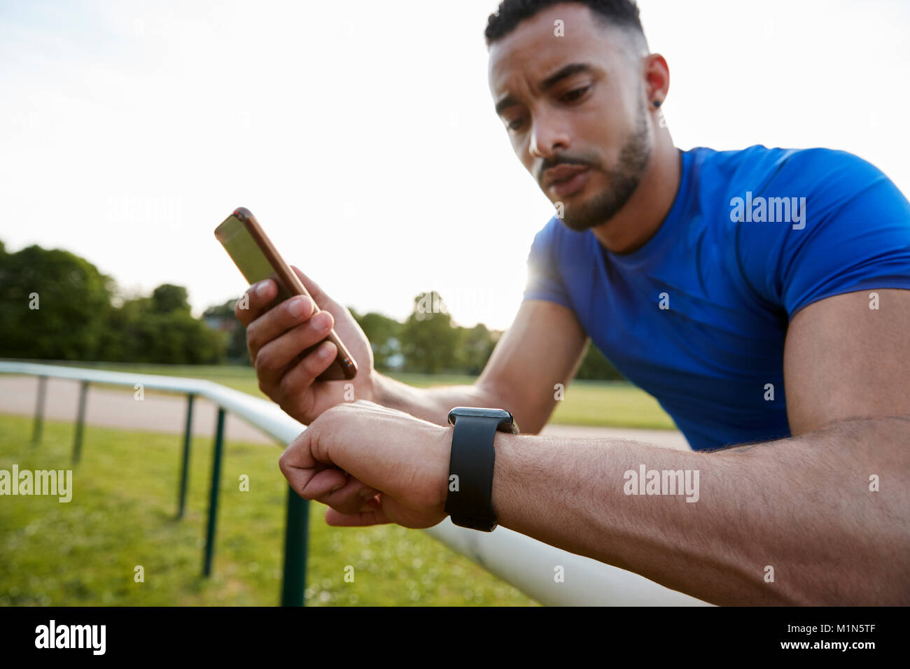 Atleta maschio utilizzando app fitness su smartphone e smartwatch Foto Stock