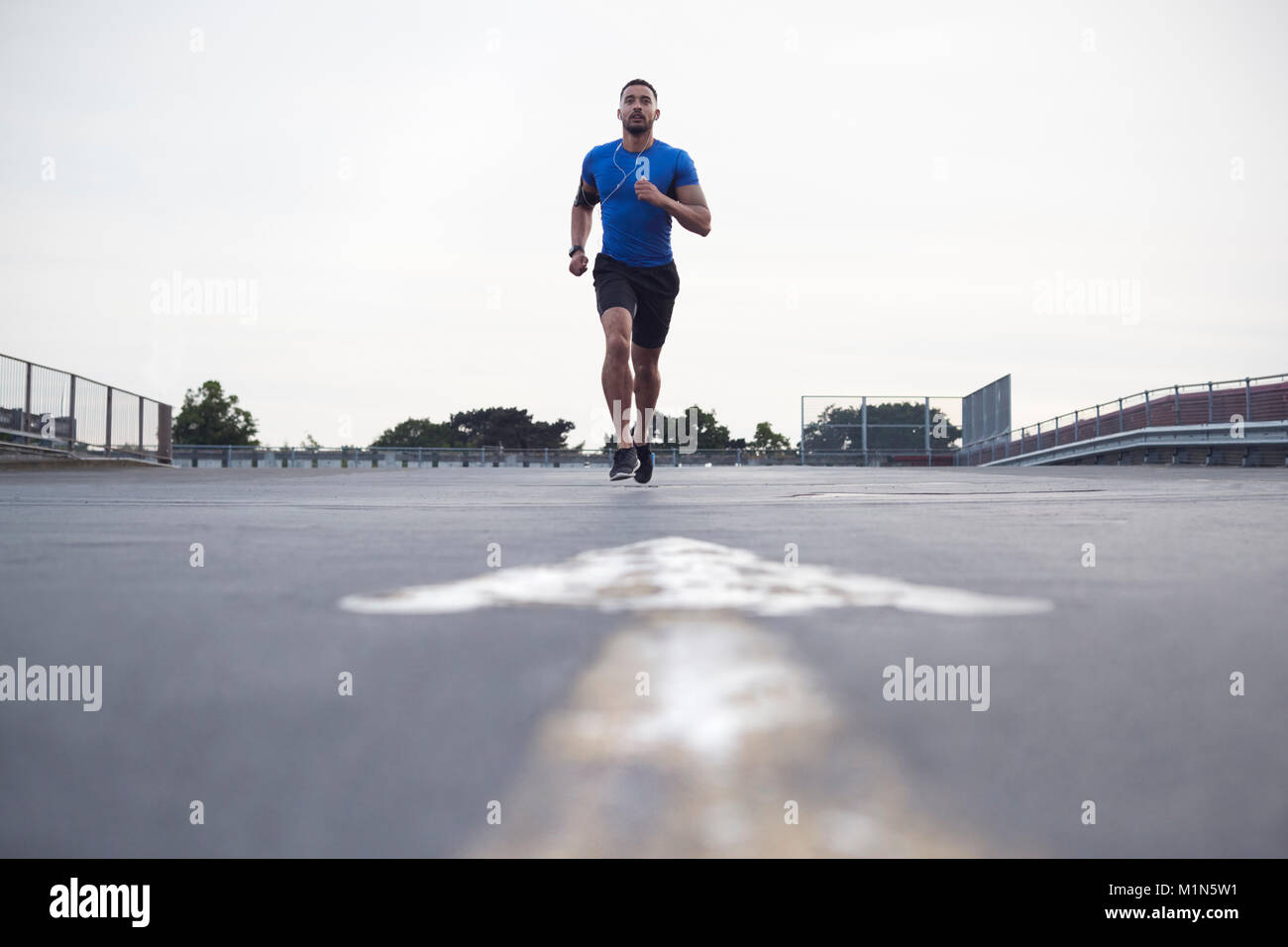 Atleta maschio in esecuzione su una strada verso la telecamera a piena lunghezza Foto Stock