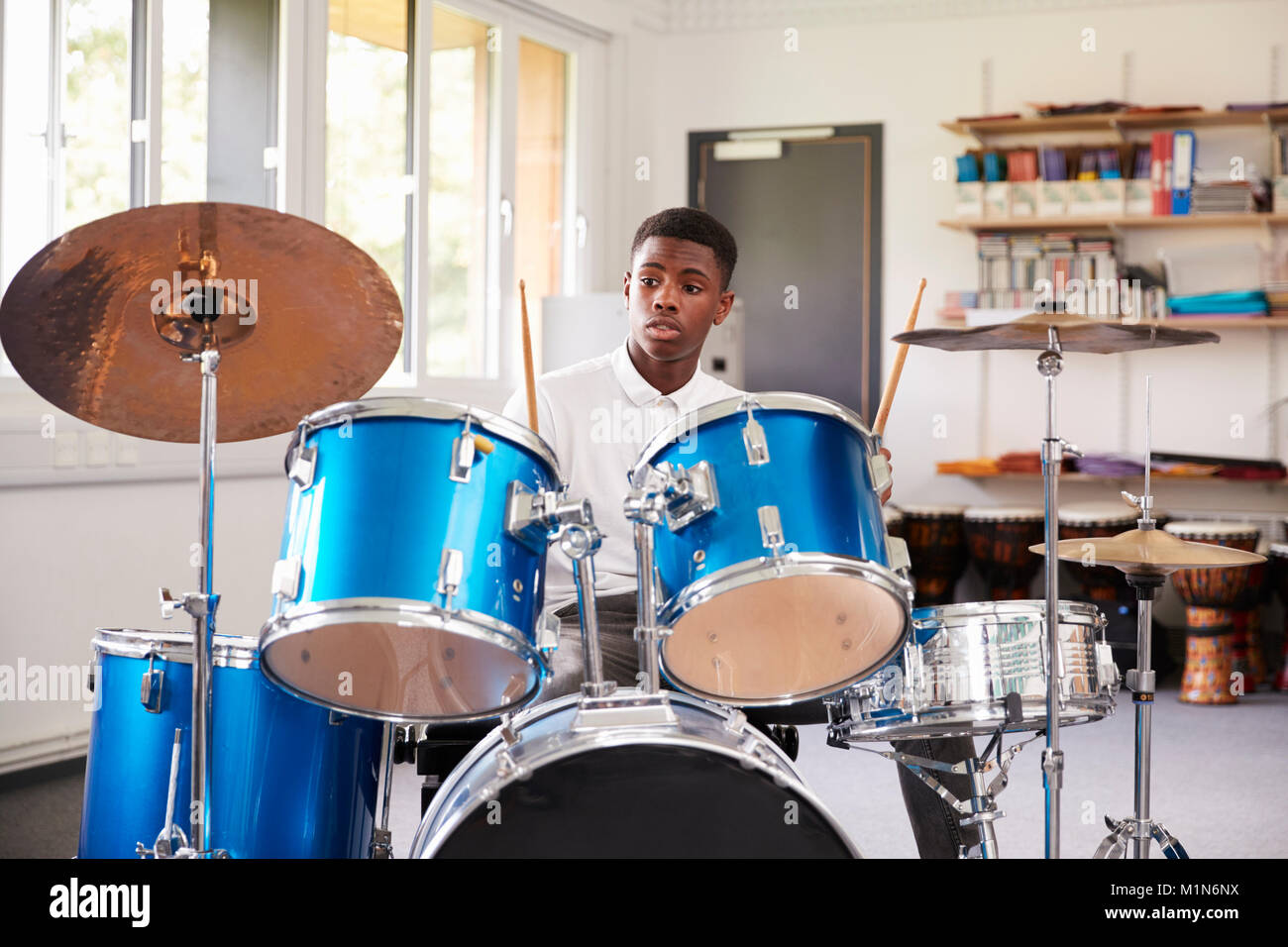 Maschio pupilla adolescente suonando la batteria In Lezione di musica Foto Stock