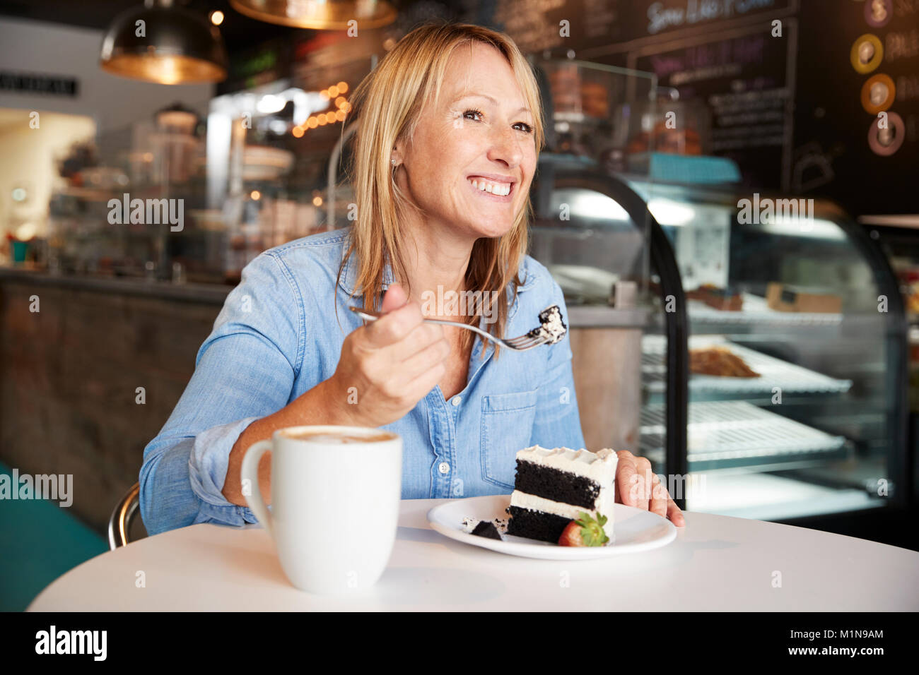 La donna nel Coffee Shop seduta a tavola a mangiare fetta di torta Foto Stock