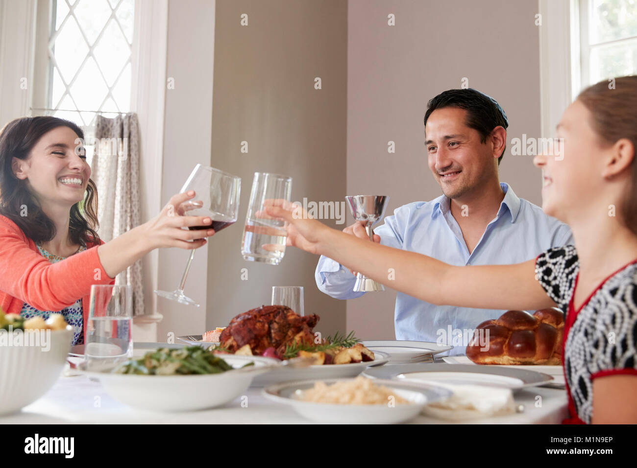 Famiglia ebraica alzando i bicchieri a tavola per la cena di Shabbat Foto Stock