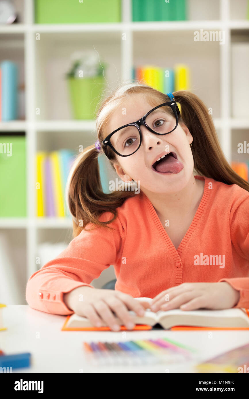 Carino divertente bambina smette di compiti a casa la lettura al suo bastone con la lingua fuori Foto Stock