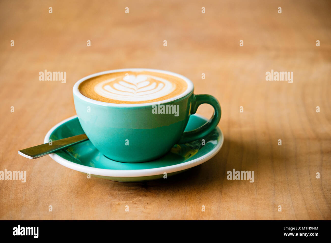 Una tazza di caffè con latte art di una foglia in schiuma con un cucchiaio su una tavola di legno Foto Stock