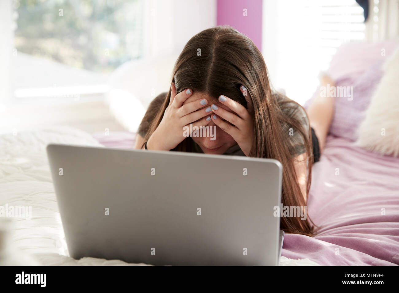 Sconvolto teen ragazza distesa sul letto con testa in mani con laptop Foto Stock