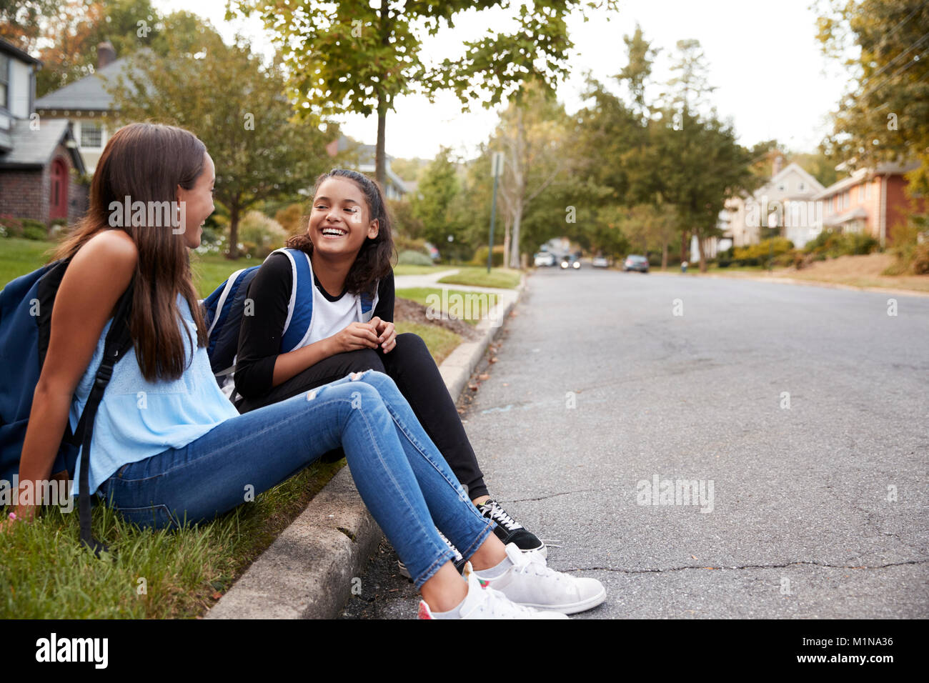 Due amiche teen sedersi a parlare al bordo della strada Foto Stock