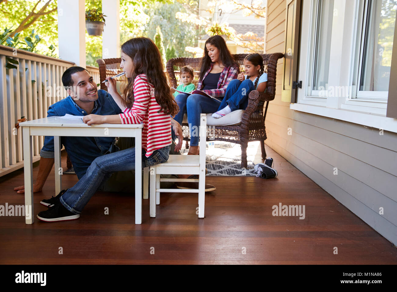 Famiglia seduti sulla veranda della casa di lettura di libri e giochi Foto Stock