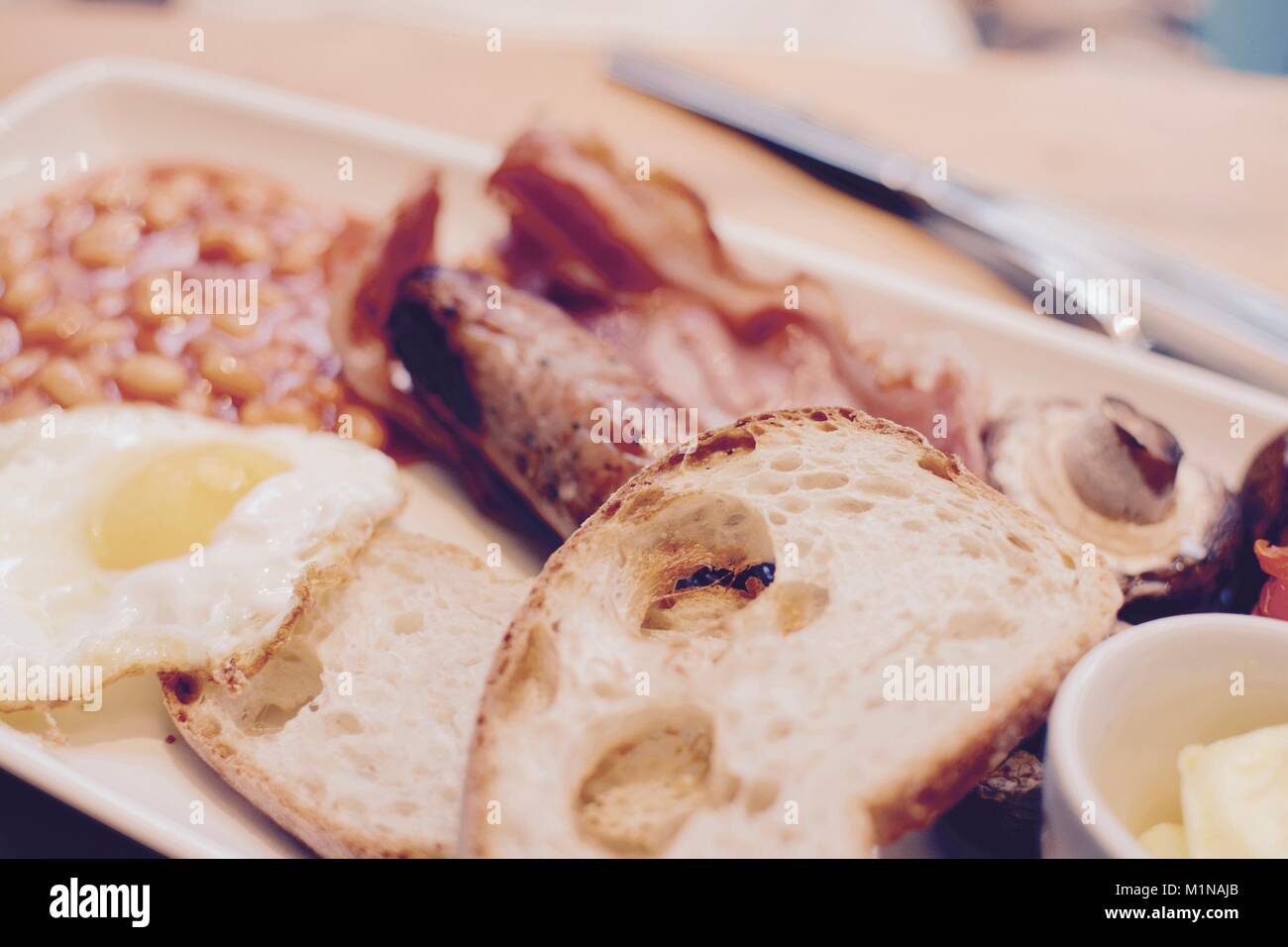 Colazione cucinata con toast, pancetta, uova fritte, salsicce, fagioli al forno, i funghi e il burro - filtro applicato Foto Stock