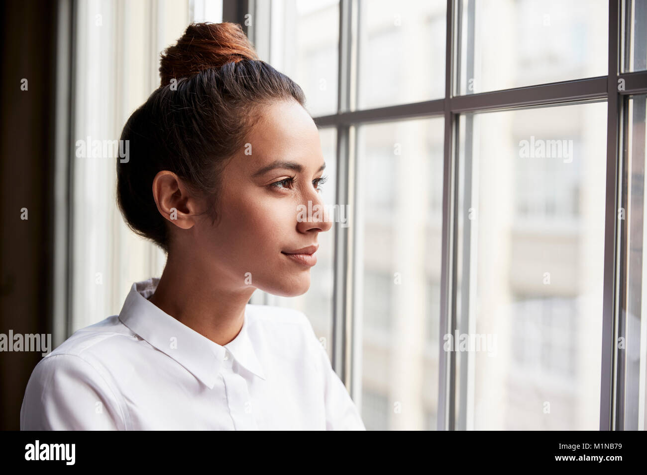 Giovane imprenditrice con capelli bun guardando fuori della finestra Foto Stock
