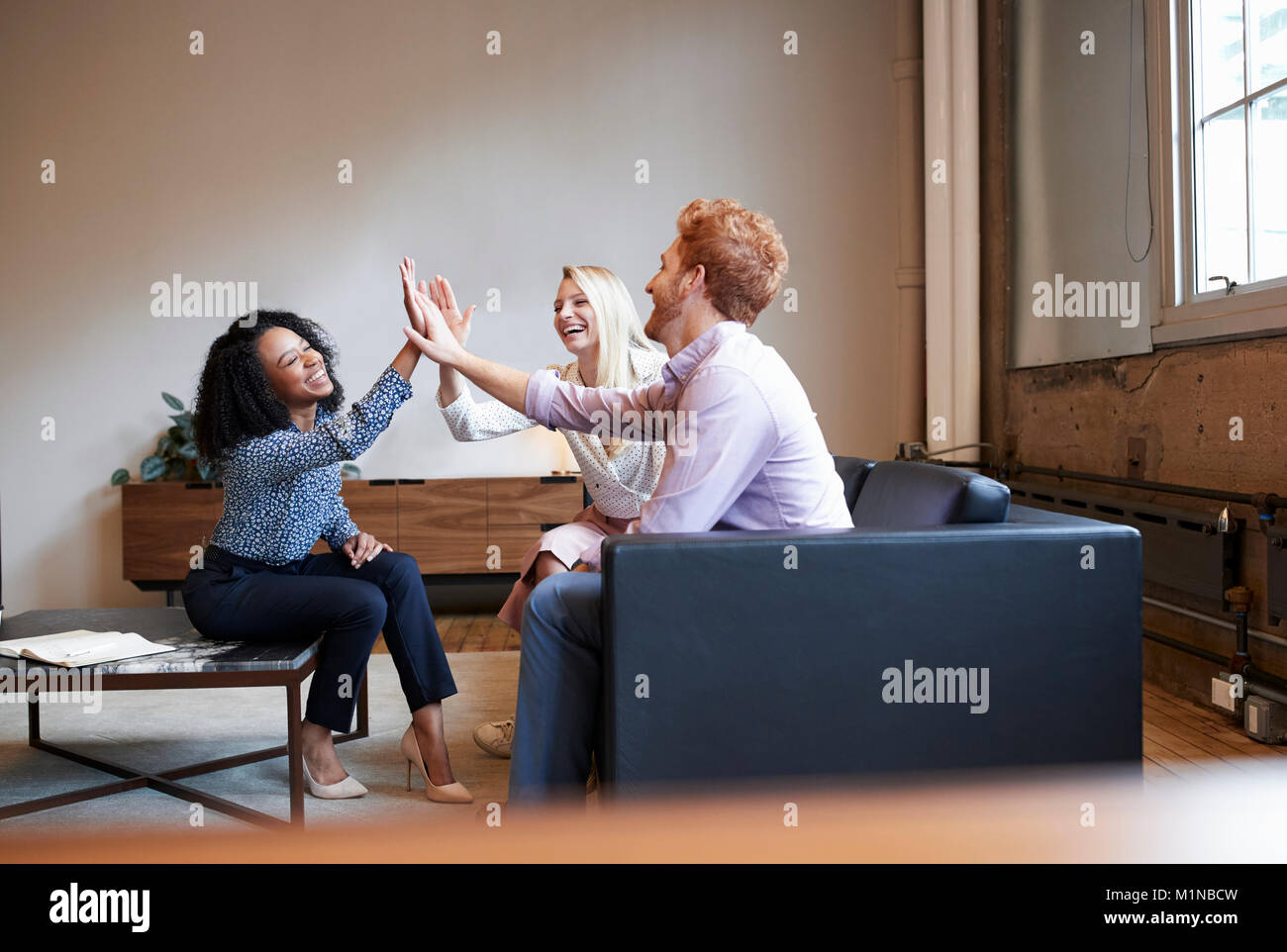 Tre colleghi alta cinque a un lavoro occasionale incontro Foto Stock