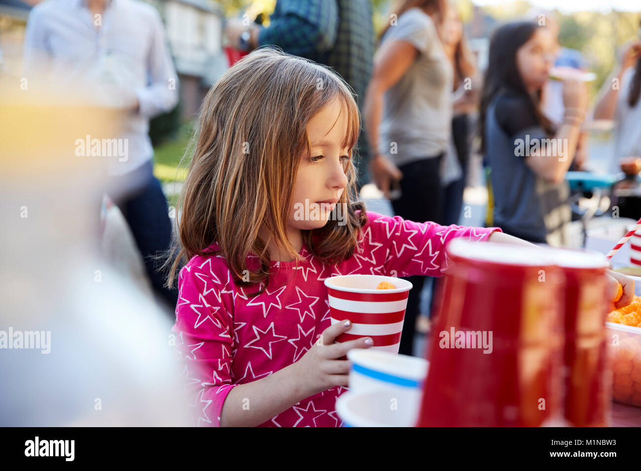 4 anno vecchia ragazza aiutare se stessa di cibo in un block party Foto Stock