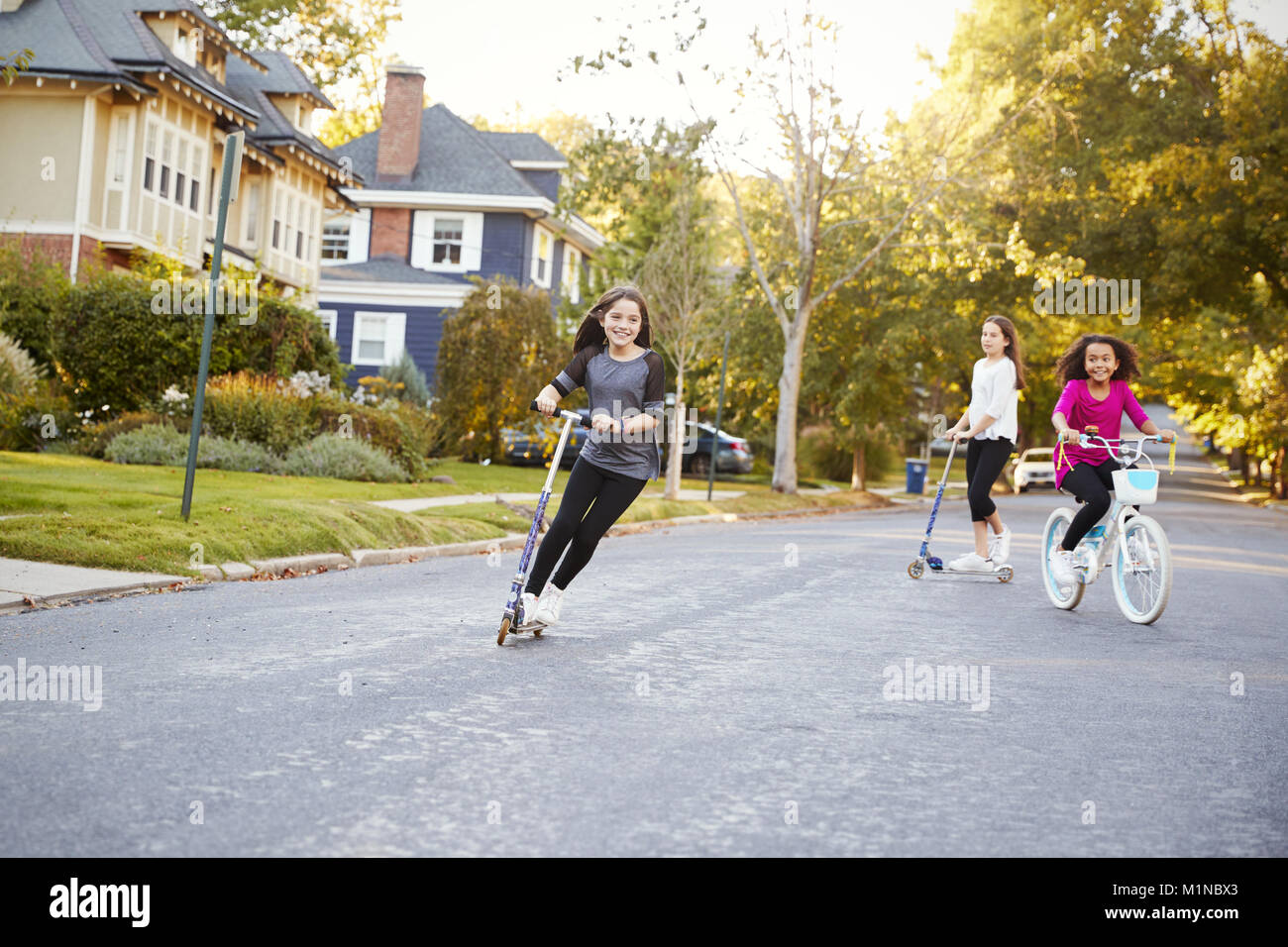 Tre pre-teen ragazze giocare in strada a scooter e moto Foto Stock