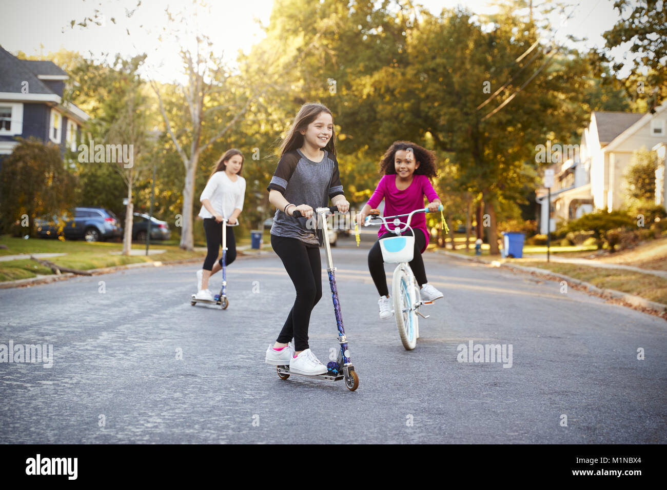 Le tre ragazze cavalcare giù lungo la strada a scooter e bici Foto Stock