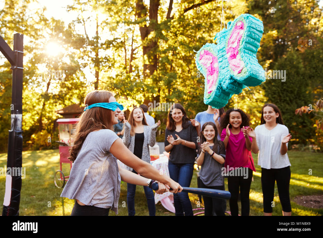 Amici guardare la pre-teen ragazza di colpire una piñata per il suo compleanno Foto Stock