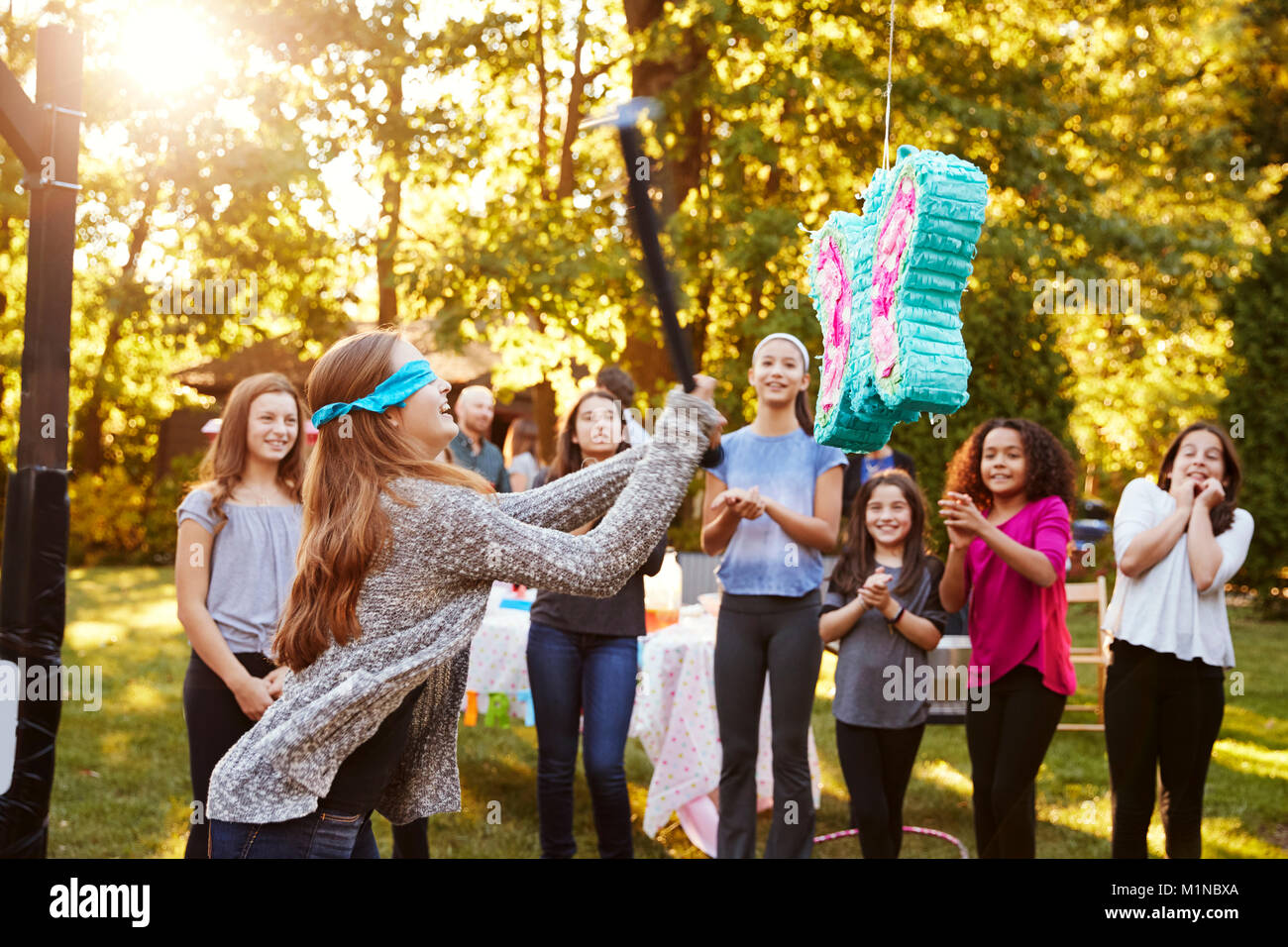 Amici guardare la ragazza adolescente di colpire una piñata per il suo compleanno Foto Stock