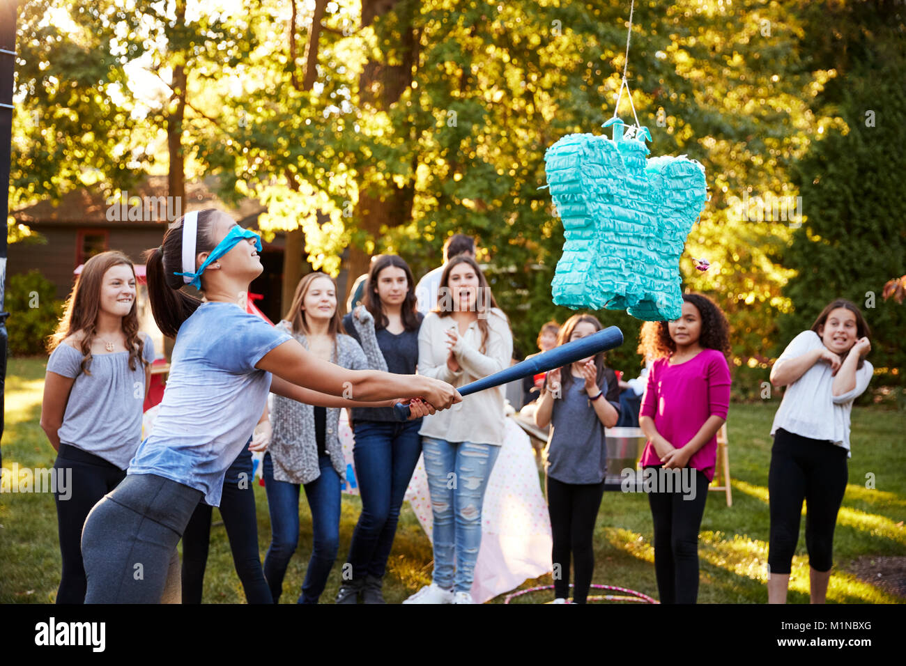 Amici guardare la ragazza adolescente di colpire una piñata per il suo compleanno Foto Stock