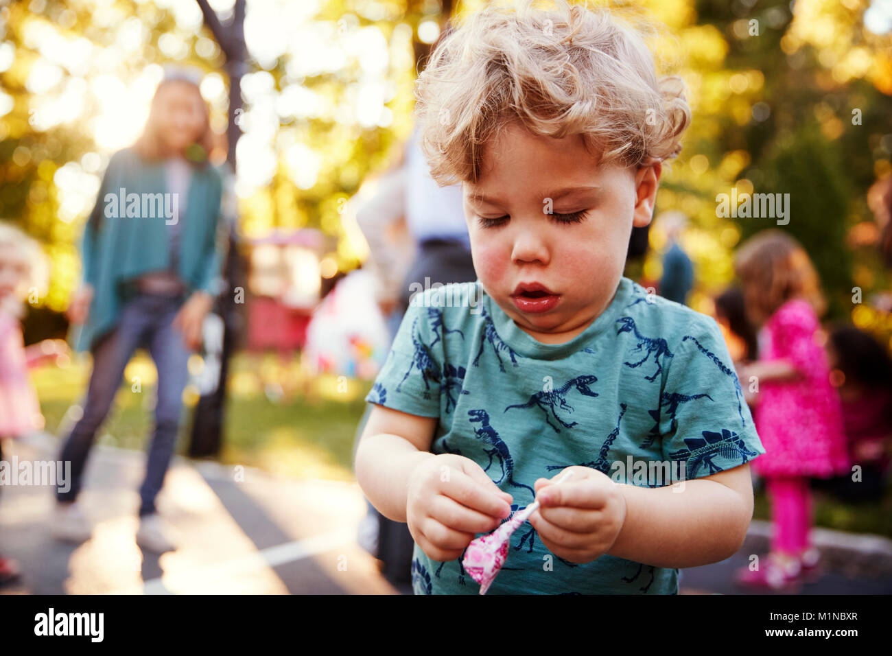 Il Toddler boy scartare un lecca-lecca all'aperto Foto Stock