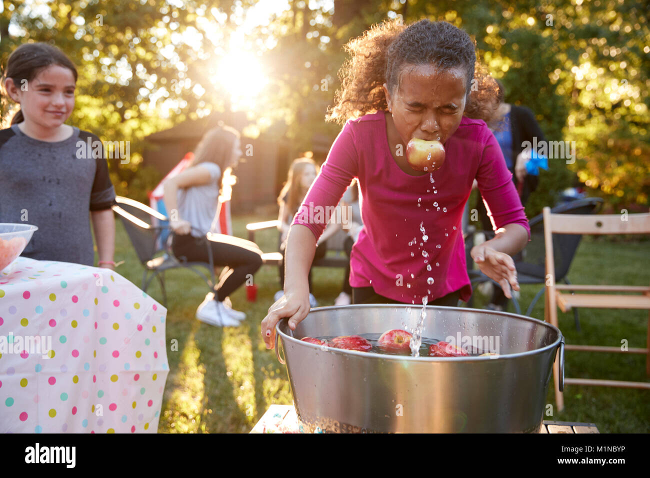 Pre-teen girl, Apple in bocca, apple bobbing al party in giardino Foto Stock