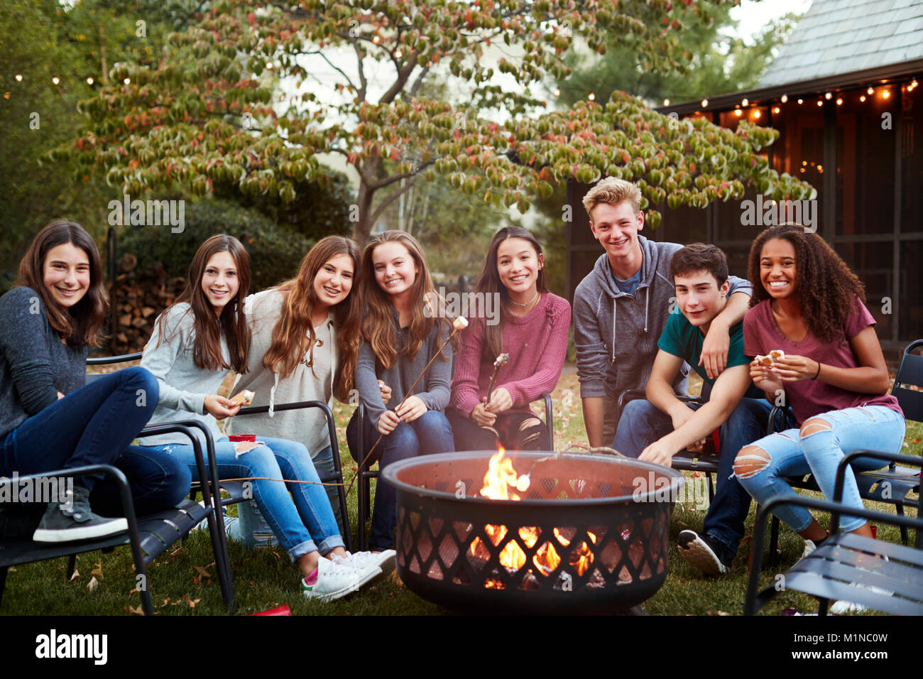 Gruppo di adolescenti seduti intorno a un falò di sorridere alla telecamera Foto Stock