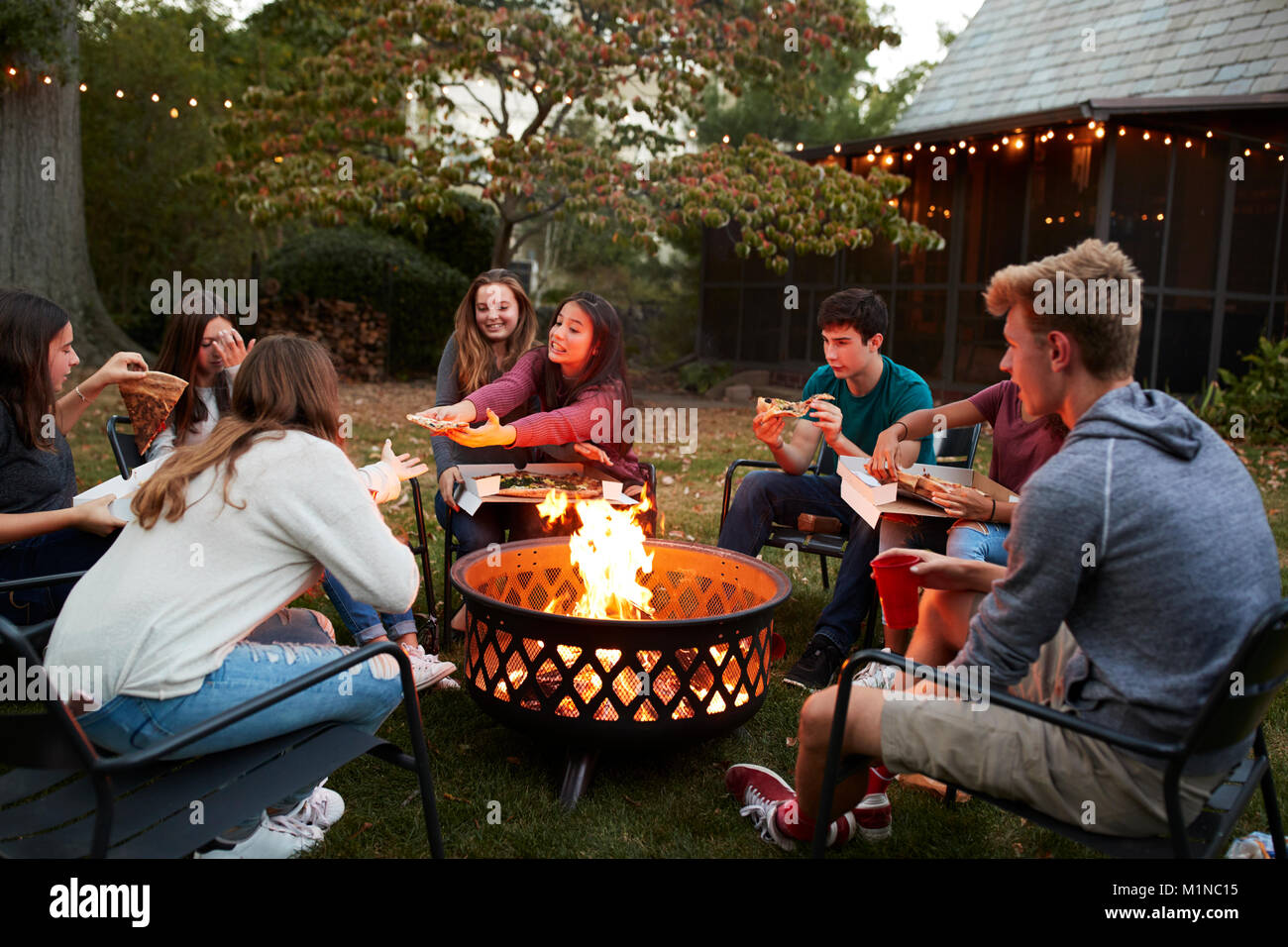Amici di adolescenti sedersi attorno a una buca per il fuoco mangiare take-away pizza Foto Stock