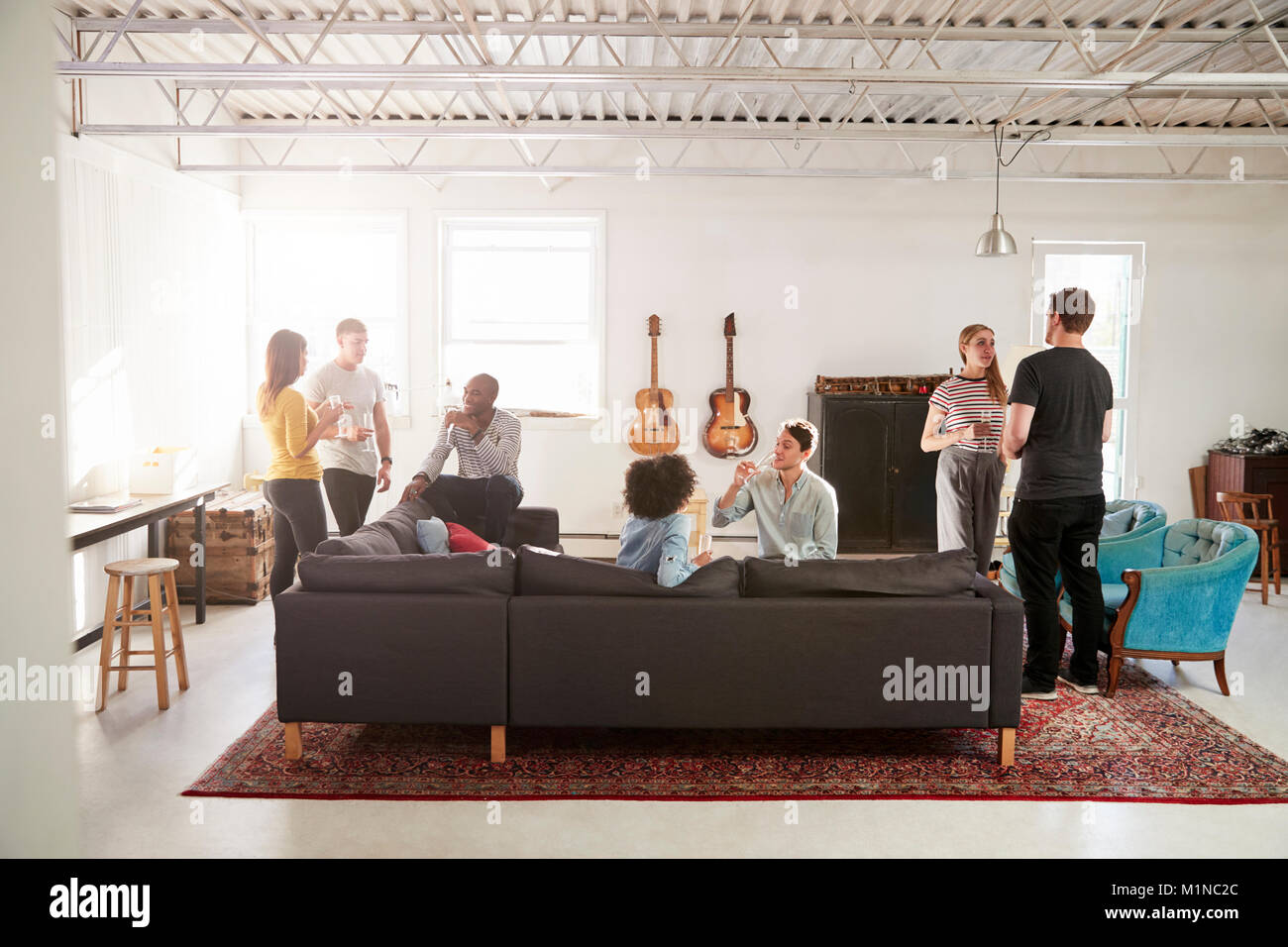 Gli amici a una festa in una New York appartamento loft a piena lunghezza Foto Stock