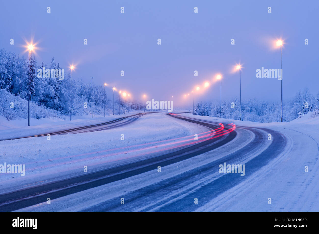 Rallentare la velocità dello shutter cattura luci di arresto di auto come una sfocatura in una fredda e nebbiosa mattina inverno lungo il fiume Eagle Loop Road in Alaska centromeridionale. Foto Stock