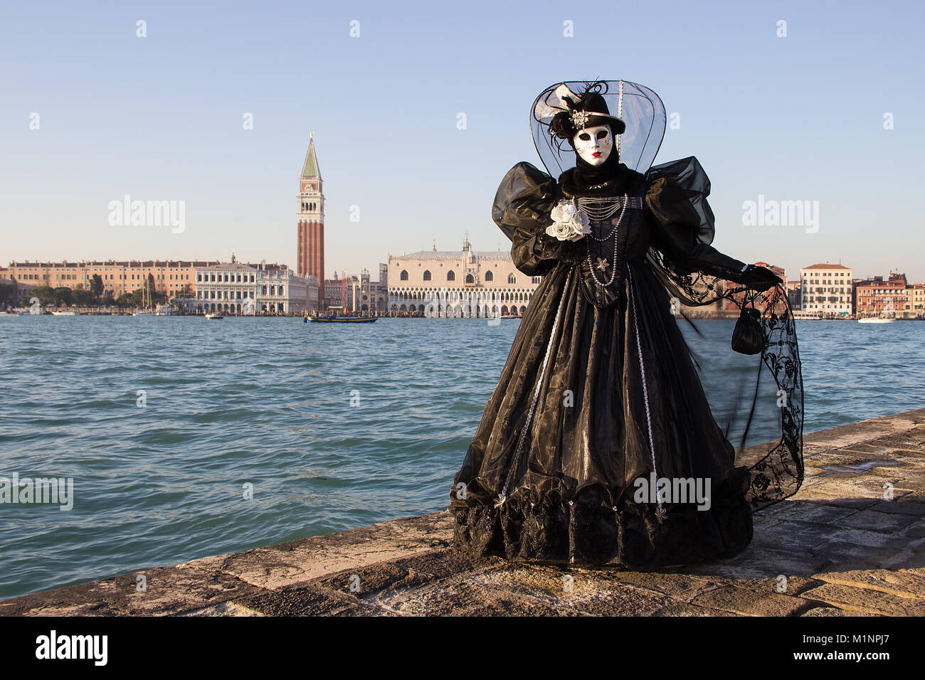 Femmina maschera veneziana in abito nero con Venezia in background, isola di San Giorgio, Venezia, Italia Foto Stock