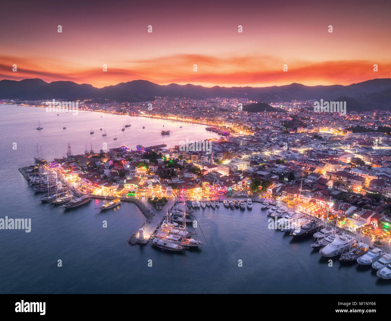 Vista aerea di barche e bella città di notte a Marmaris, Turchia. Un paesaggio fantastico con barche in marina bay, mare, luci della città, montagne, red sky Foto Stock