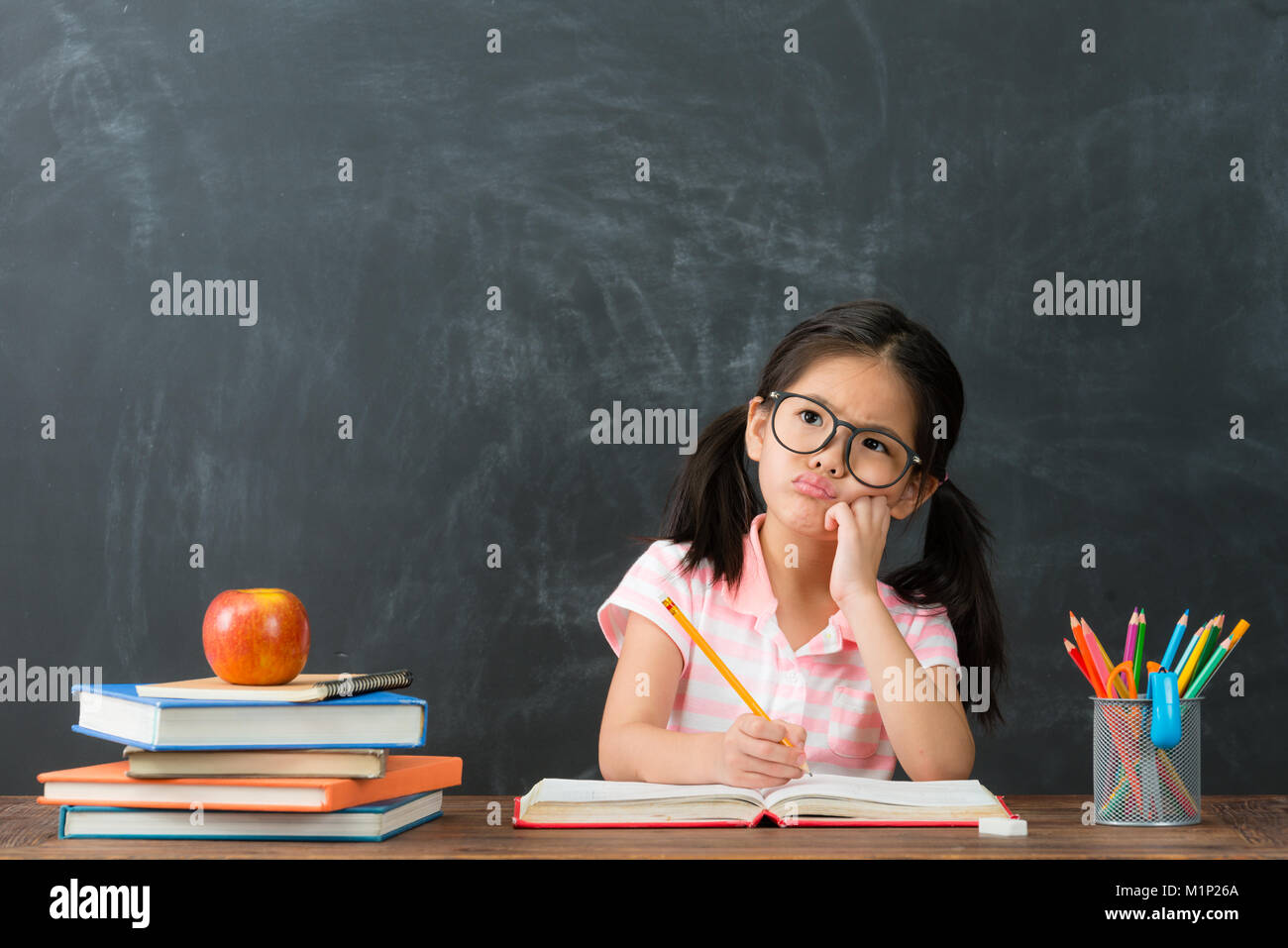 Bella femmina carino bambini compiti di scrittura avente il problema e pensando di soluzione sensazione difficoltà di lavagna sfondo. Foto Stock