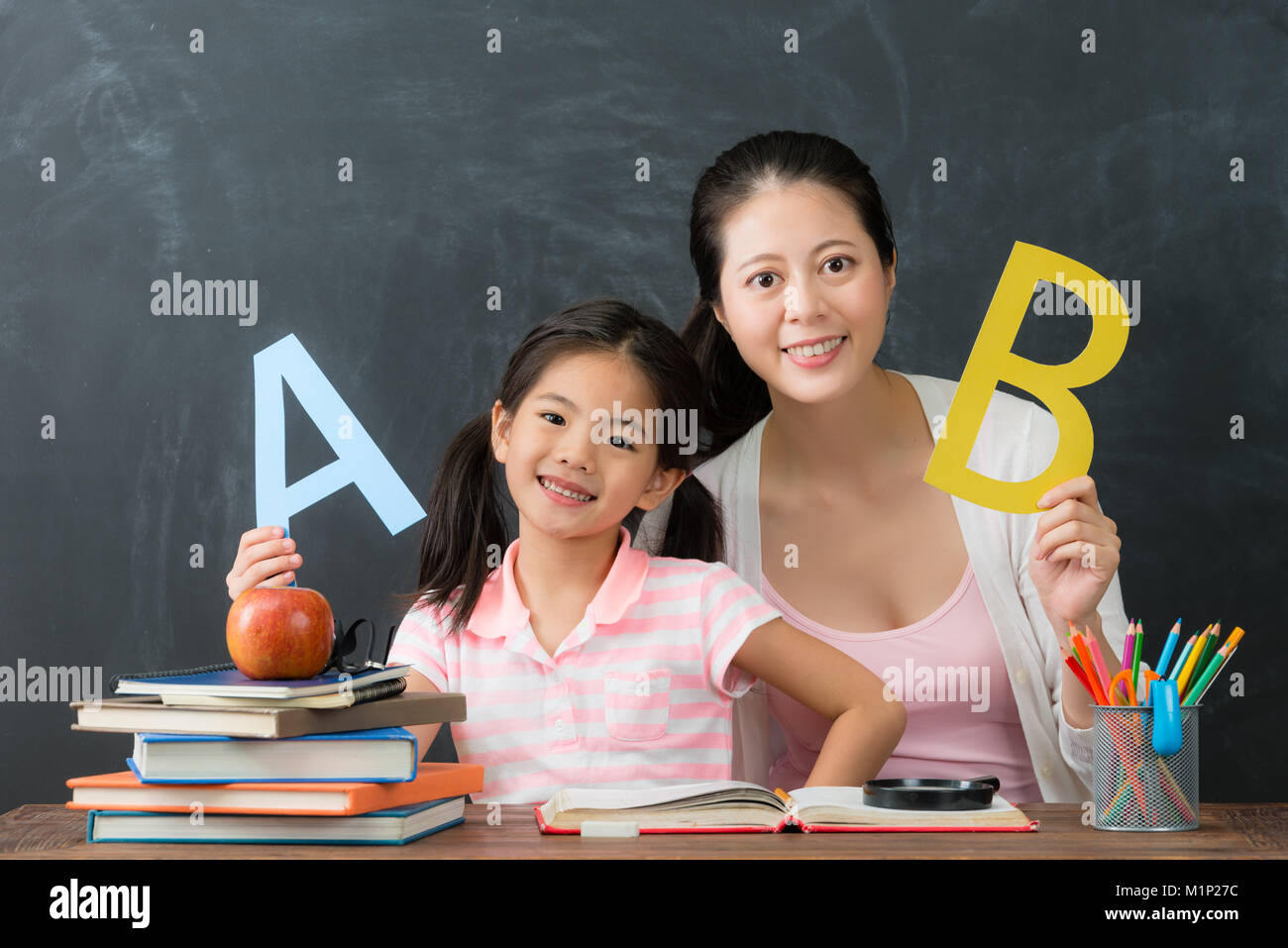 La famiglia felice di mamma con figlia studiare inglese insieme e guardando la fotocamera in background blackboard. torna al concetto di scuola. Foto Stock