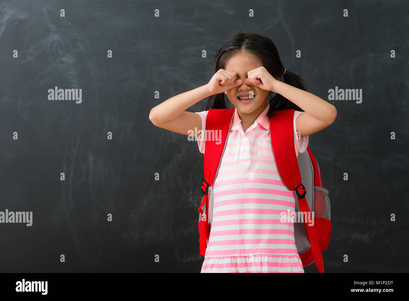 Piuttosto giovane capretto femmina i bambini non piace studiare in piedi in background della lavagna di piangere quando si ha bisogno di ritorno a scuola di apprendimento. Foto Stock