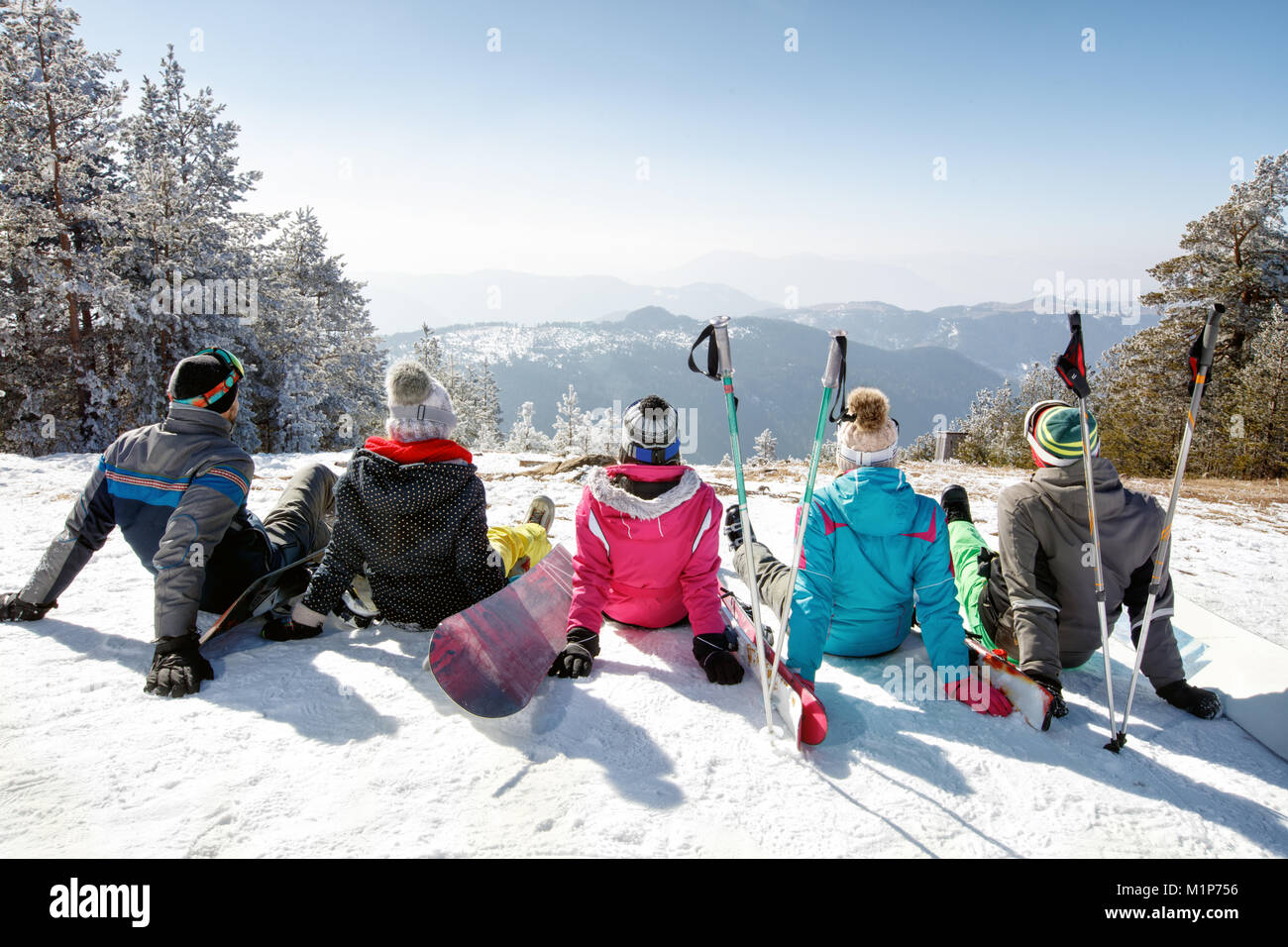 Gruppo di sciatori seduti sulla neve e guardando lo splendido paesaggio, vista posteriore Foto Stock