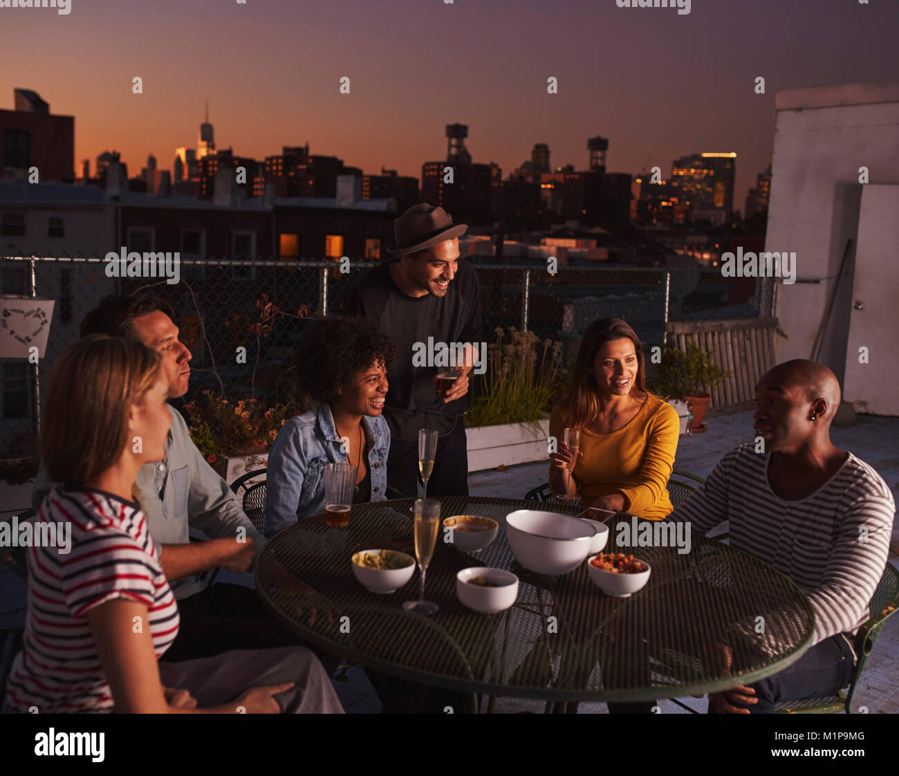 Amici adulti parlando a una tabella su un tetto, sera Foto Stock