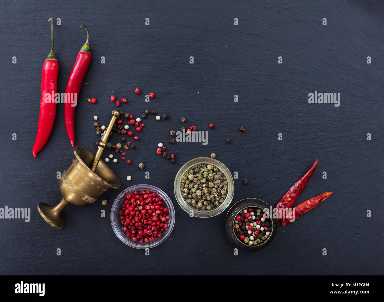 Varie grani di pepe e peperoni e pepe in ottone mulino in pietra nera di sfondo, vista dall'alto, spazio di copia Foto Stock