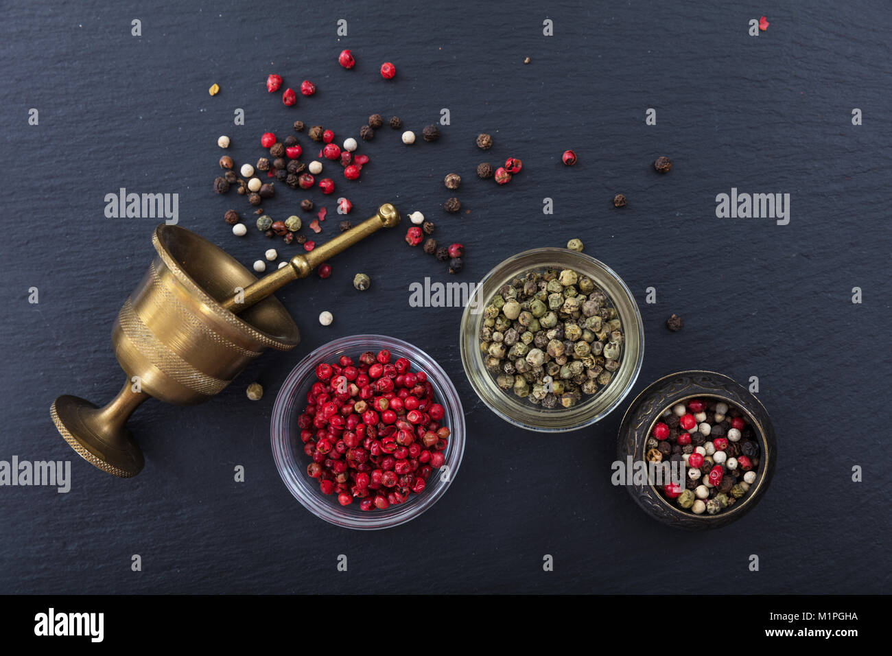Vari semi di pepe e ottone un mortaio e pestello in pietra nera di sfondo, vista dall'alto, spazio di copia Foto Stock