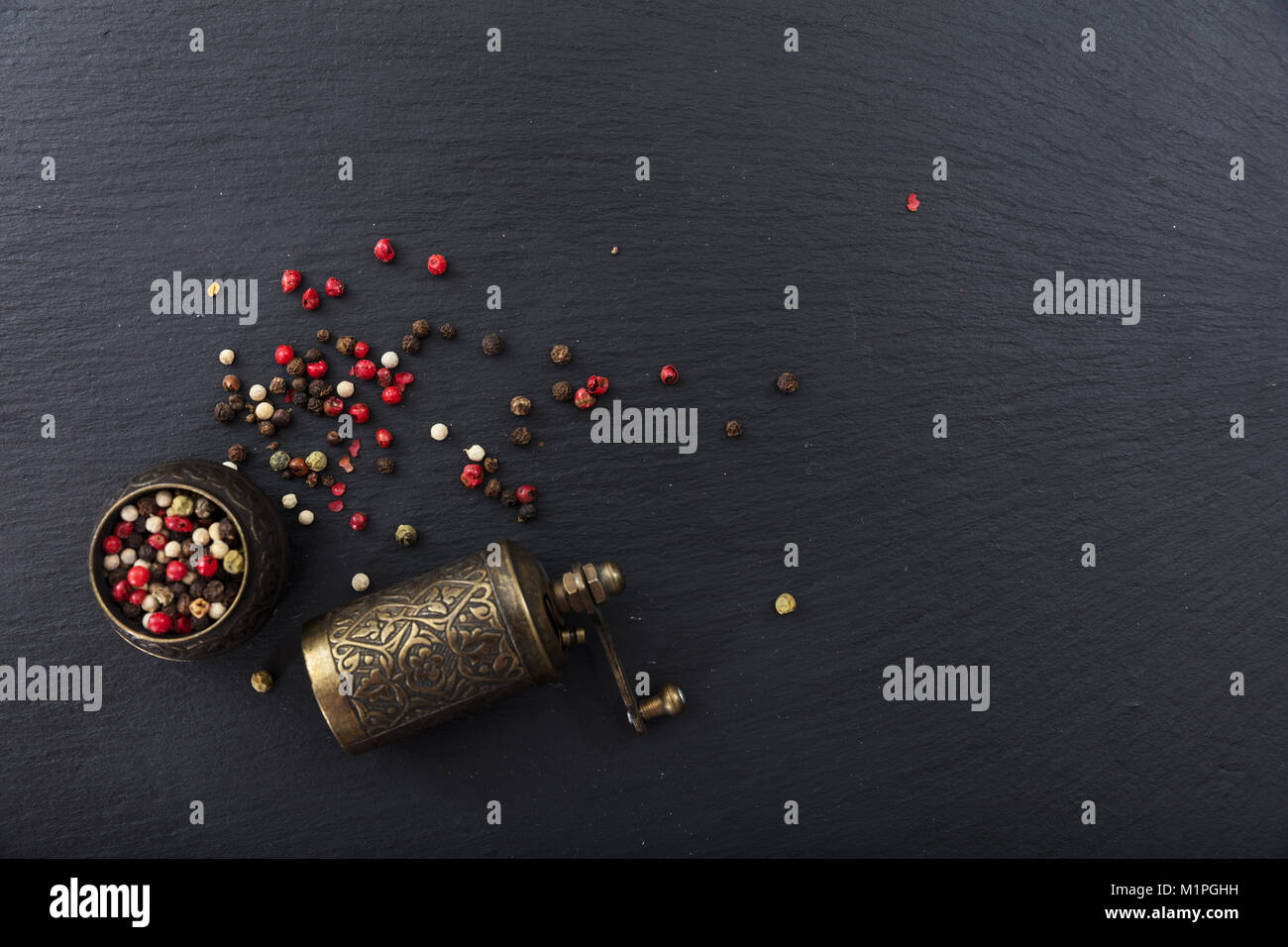 Vari semi di pepe e un pepe in ottone mulino in pietra nera di sfondo, vista dall'alto, spazio di copia Foto Stock