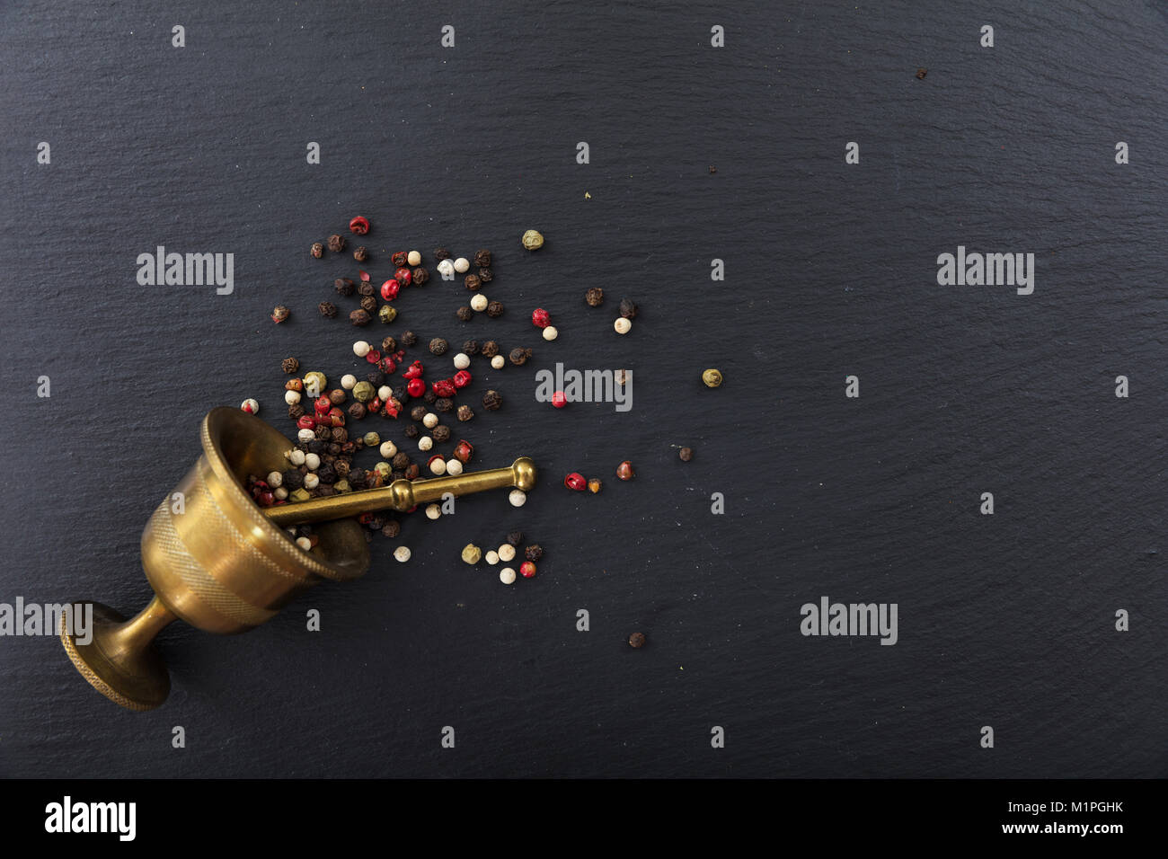 Vari semi di pepe e un mortaio di ottone sulla pietra nera di sfondo, vista dall'alto, spazio di copia Foto Stock