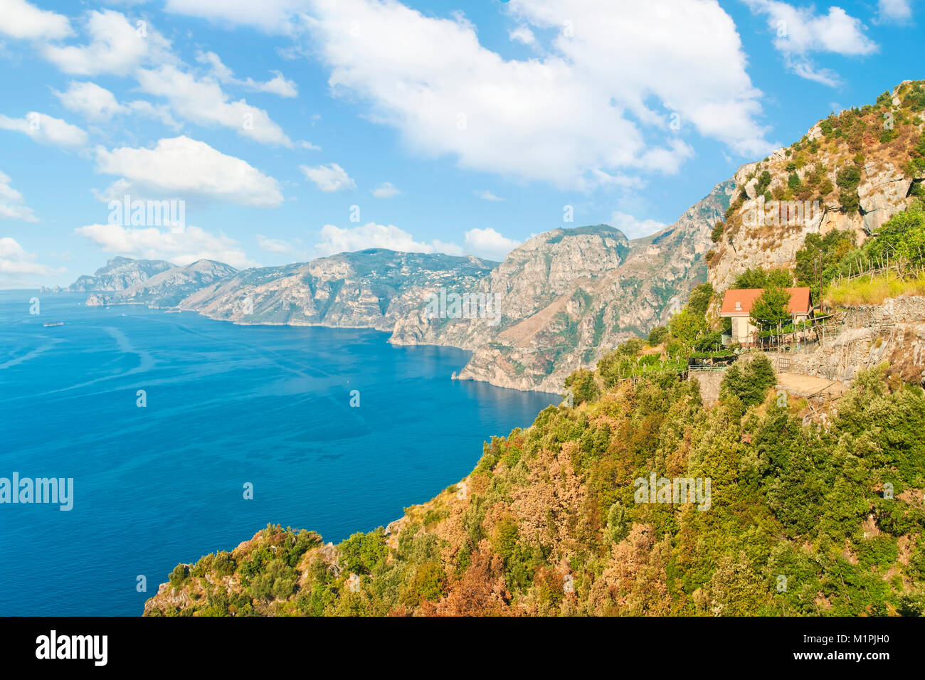Vista della piccola casa di campagna sul bordo della scogliera con la gamma della montagna a sfondo sul percorso degli dèi escursionismo via lungo la Costiera Amalfitana sulla soleggiata mattina d'estate Foto Stock