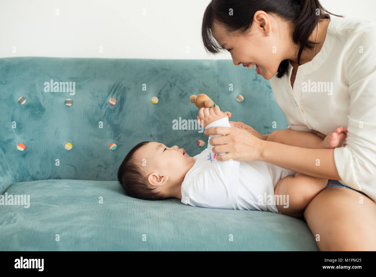 Il bambino e la madre figlia gioca, avvolgente, kissing a casa sul lettino Foto Stock