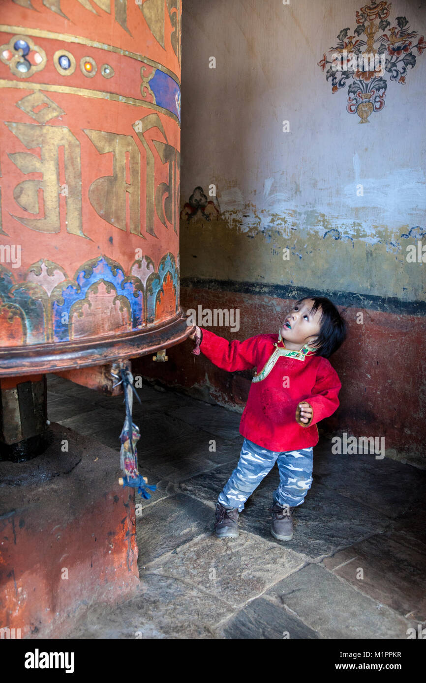 Bumthang, Bhutan. Little Boy tirando grande ruota di preghiera, Jambay Lhakhang monastero. Foto Stock